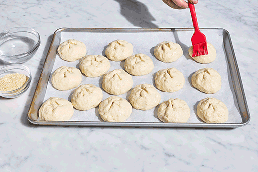 Brushing the top of gluten-free dough with water and sprinkling toppings on them.
