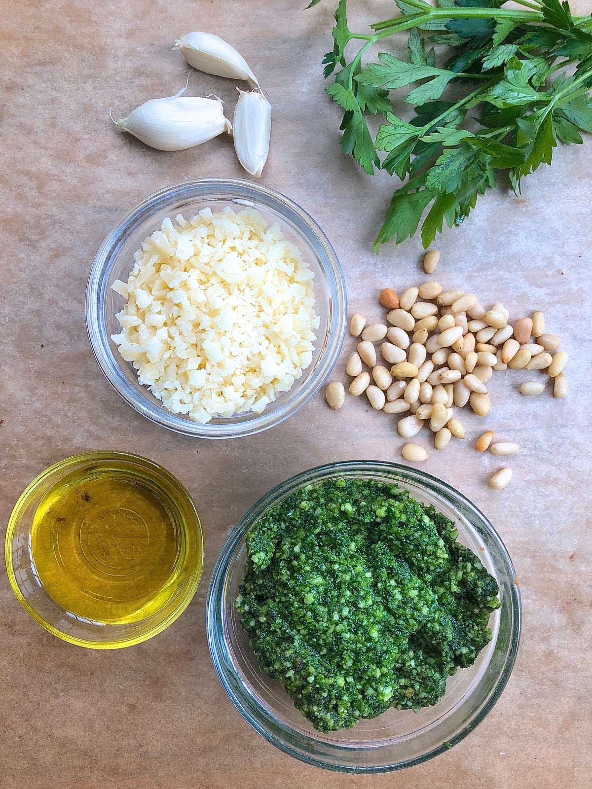 Ingredients for pesto sauce, incouding parsley, grated Parmesan, olive oil, pine nuts, and garlic cloves