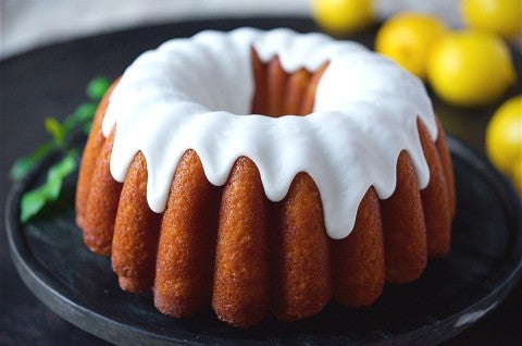 A side angle photo of Glazed Lemon Bundt Cake. The cake has a thick white glaze on top that is delicately dripping down the sides of the cake. - select to zoom