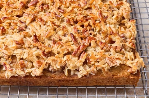 Oatmeal Cake photographed on a baking rack from the side to show a dark brown cake edge and layer of pecans, coconut, and more oats as a crunchy, toasty cap. - select to zoom