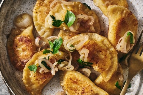 Homemade Pierogis on a plate with perfectly browned exteriors, garnished with herbs and onions. - select to zoom