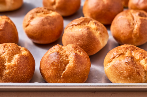 Freshly baked gluten-free rolls on a sheet tray with split tops and a deep golden crust. - select to zoom