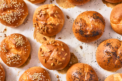 Freshly baked gluten-free rolls and buns on a sheet tray with split tops and a deep golden crust. - select to zoom