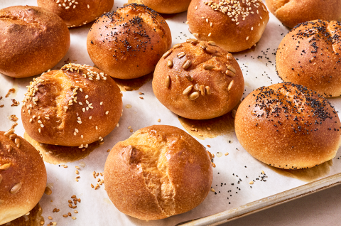 Freshly baked gluten-free rolls on a sheet tray with split tops and a deep golden crust. - select to zoom