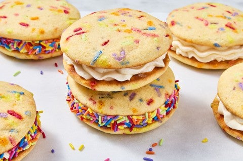 Confetti Whoopie Pies stacked on a counter with sprinkles decorating the filling around the outside of the whoopie pies. - select to zoom