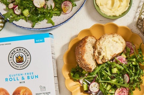 A Gluten-Free Seeded Hearth Roll on a plate with a box of Gluten-Free Roll & Bun mix. - select to zoom