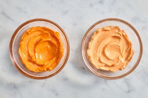Small bowl of brighter orange frosting next to a small bowl of pale orange frosting 