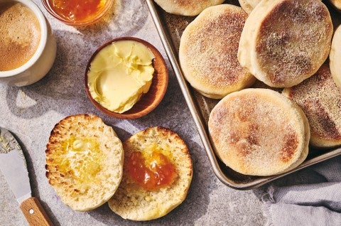 A sliced Sourdough English Muffin on a counter with butter and jam and several others on a sheet tray - seen from above - select to zoom
