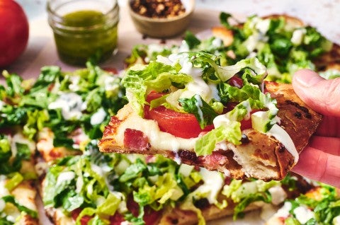 A slice of BLT Pizza shown from the size with tomatoes, bacon, and fresh chopped lettuce - select to zoom