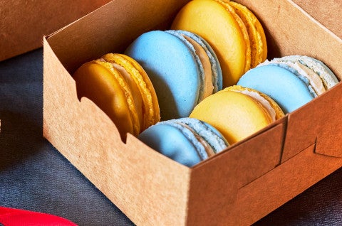 Yellow and blue macarons layered in a cardboard container. - select to zoom