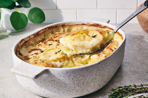 Scalloped potatoes being scooped out of a stoneware pan with a spoon - select to zoom
