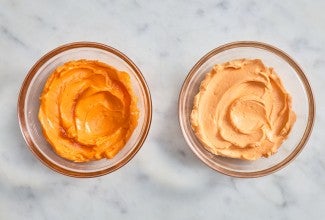 Small bowl of brighter orange frosting next to a small bowl of pale orange frosting 