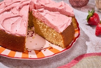 Brown Sugar Strawberry Frosted Cake seen from the side showing a thick layer of frosting and a golden cakey interior.