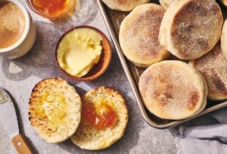 A sliced Sourdough English Muffin on a counter with butter and jam and several others on a sheet tray - seen from above