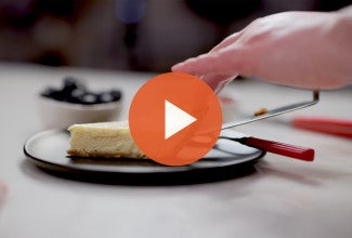Putting a slice of easy cheesecake on a plate with an orange play icon over the image - select to zoom