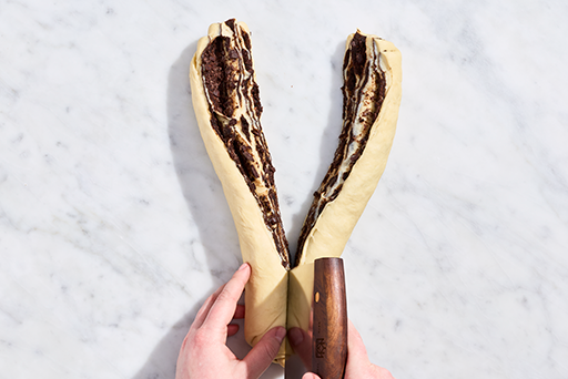 Chocolate Sourdough Babka dough being cut down the middle with a bench knife.