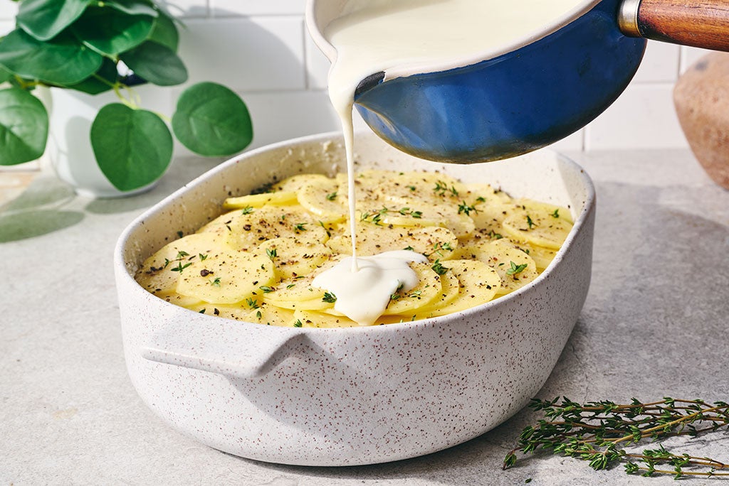 Pouring sauce over scalloped potatoes before baking them