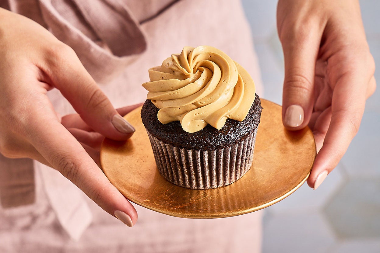 Holding a plate with a Chocolate Cupcake with Whipped Caramel Frosting on it