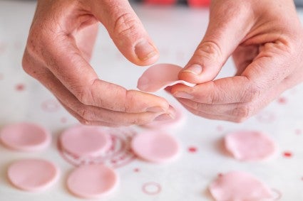 A baker pressing the edges of modeling chocolate circles to make them look like petals