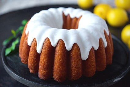 A side angle photo of Glazed Lemon Bundt Cake. The cake has a thick white glaze on top that is delicately dripping down the sides of the cake.