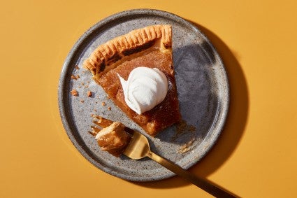 A slice of Maple Cream Pie on a plate topped with whipped cream with a bite on a fork