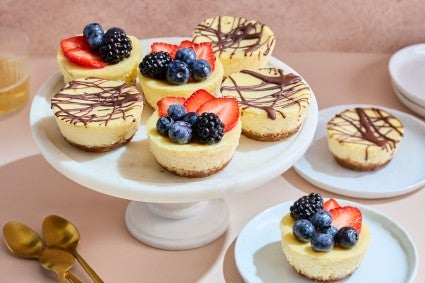 Mini Cheesecakes arranged on a pedestal and plates with fresh berries and chocolate drizzle topping them.