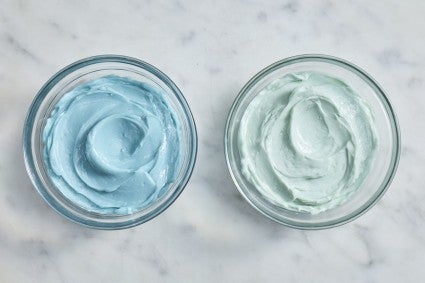 Small bowl of brighter blue frosting next to a small bowl of pale blue frosting 
