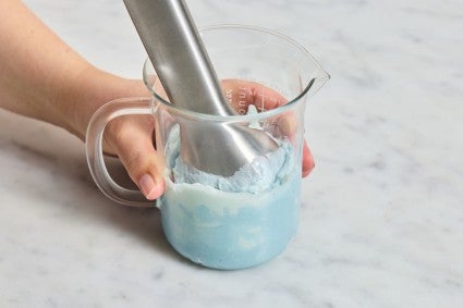 Blue colored frosting being beaten with an immersion blender 