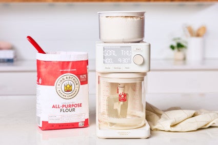 The Sourdough Sidekick, an automatic sourdough feeder, next to a bag of flour