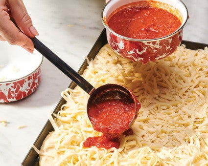 Saucing a pizza, with grated cheese beneath 