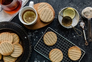 A batch of Digestive Tea Biscuits on a cooling rack with a couple cups of tea