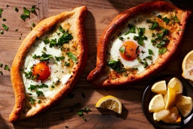 Two freshly baked Khachapuri (Georgian Cheese Breads) topped with soft-baked eggs and fresh herbs