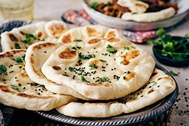 Several pieces of freshly cooked naan on a plate, garnished with herbs and ghee