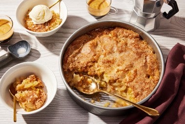 A round pan of Sugar-Crusted Apple Cobbler with a spoonful portioned into a small bowl.
