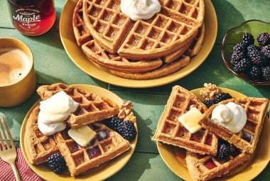 Gingerbread Waffles on a green countertop with some on plates and others stacked.