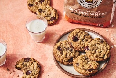 Whole Wheat Oatmeal Cookies on a plate with a glass of milk and a cookie with a bite taken out on a counter seen from above