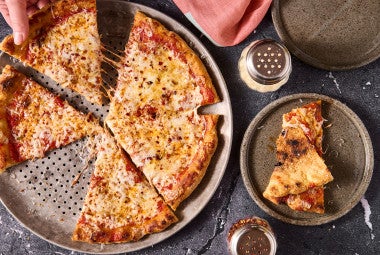 A Gluten Free NY Style Pizza on a pizza pan seen from above.