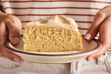A slice of Frosted Brown Butter Cake being held on a plate seen from the side